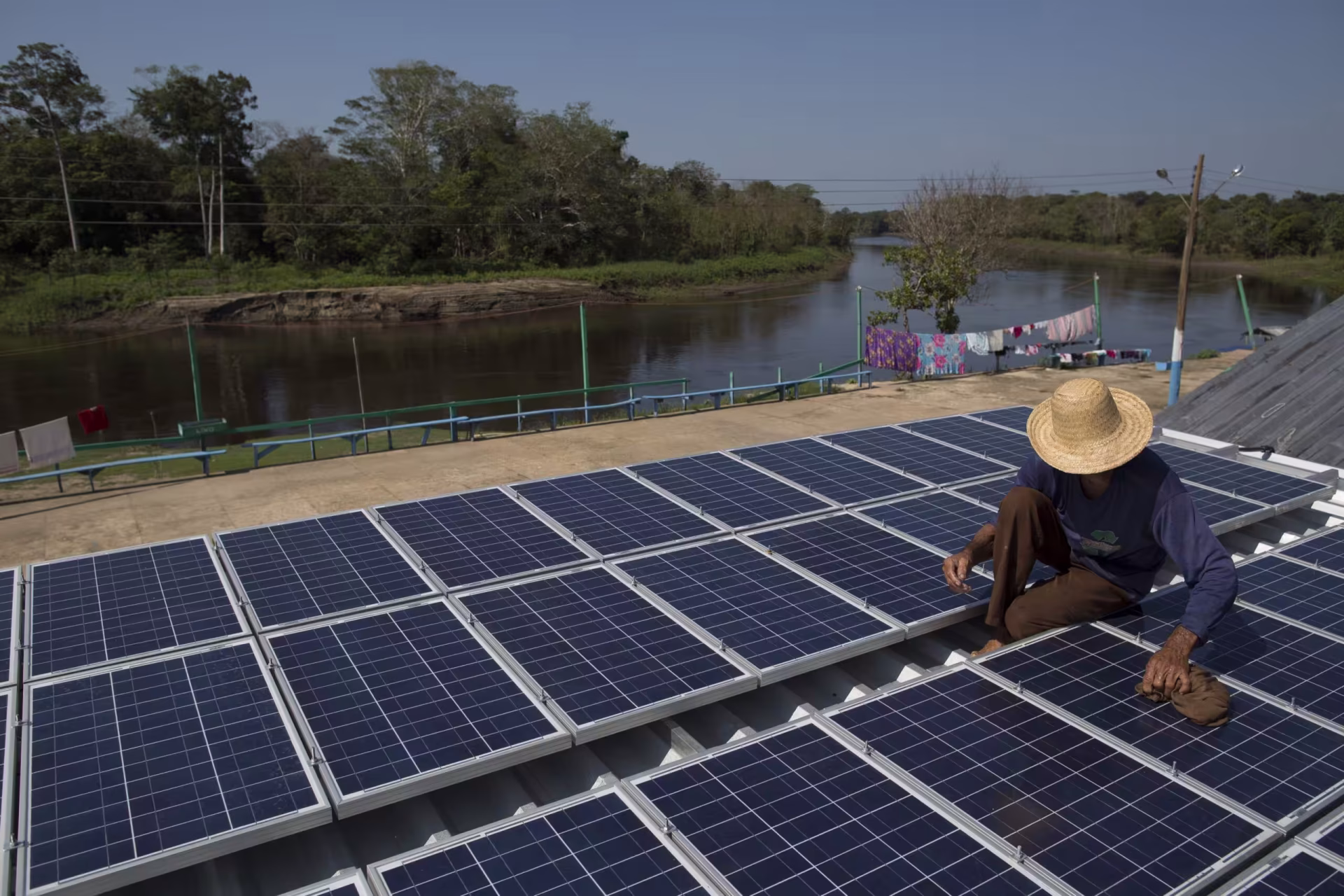 Módulos fotovoltaicos instalados sobre um telhado à beira do rio, com uma pessoa fazendo a instalação