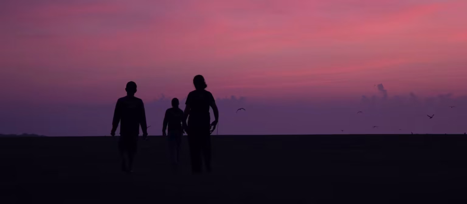 Silhuetas de pessoas caminhando em uma praia ao entardecer, sob céu rosado